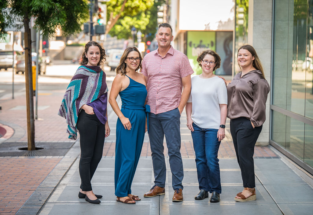 group photo of employees standing on sidewalk with city scene behind them