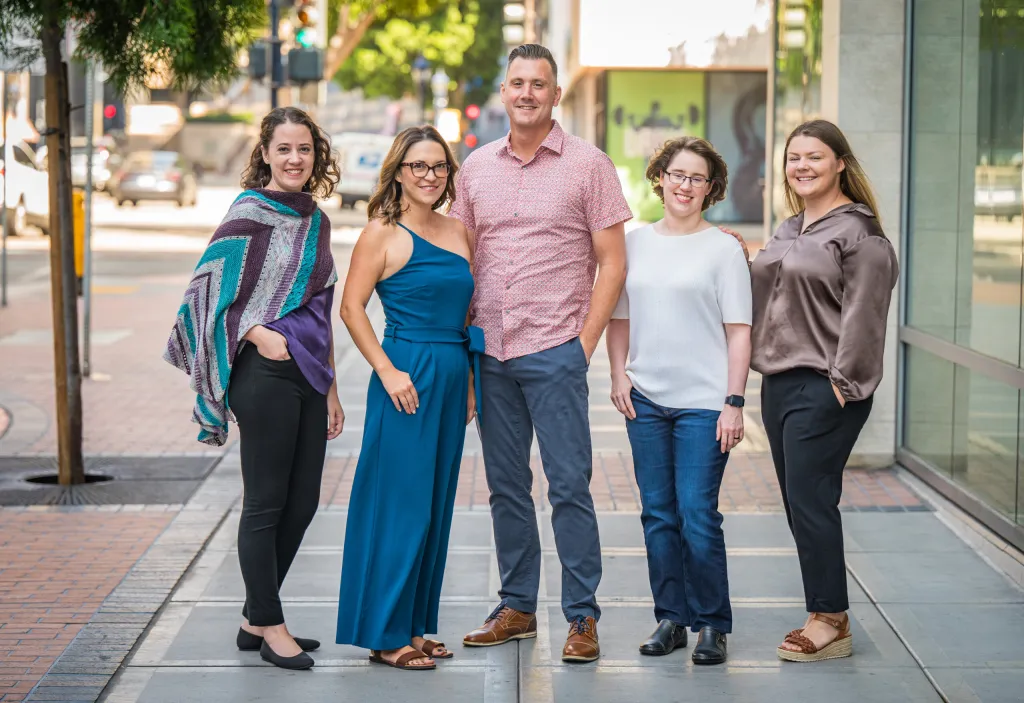 group photo of employees standing on sidewalk with city scene behind them